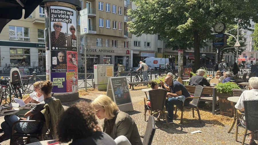 Plakat der Kampagne an einer Litfaßsäule neben einem belebten Berliner Cafe